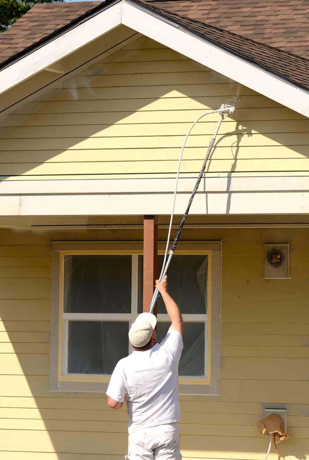 A painting contractor uses a extension on his spray gun to paint a overhang on a commercial residential development